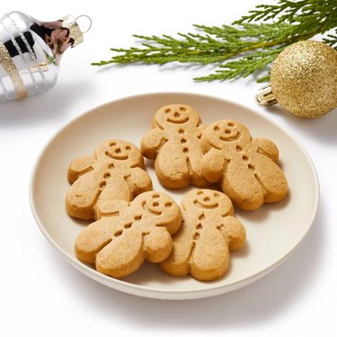 A plate of five gingerbread cookies on a white surface with Christmas ornaments in the background.