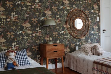 Green forest animal wallpaper in kids room with plaid bedding, green lamp, and wicker mirror
