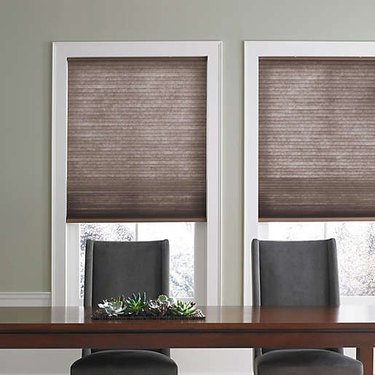A dining room table with brown cellular shades installed on the windows