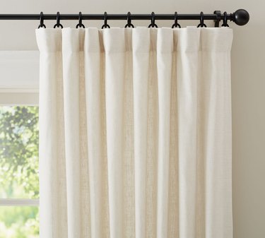 A white curtain on a black curtain rod with curtain rings