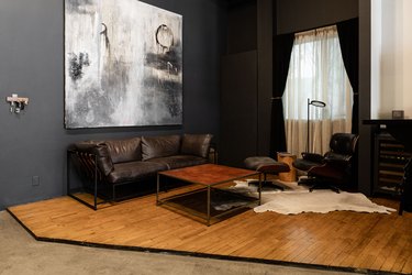 Industrial living room with black walls, abstract art, black sofa, square coffee table, black curtains, animal skin rug, black leather chair.