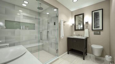 A Kohler wall-hung toilet in a bathroom with a wood vanity and a large walk-in glass shower