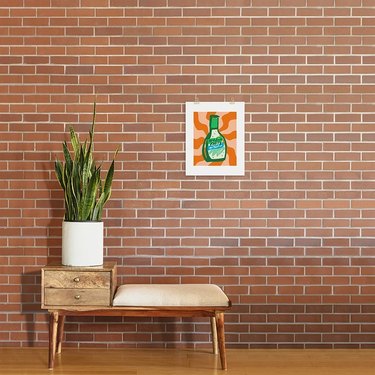 Hidden Valley Ranch art print hanging on a brick wall behind a wooden bench with a plant on top.