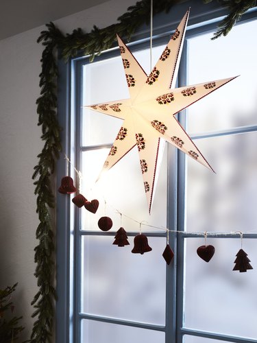 A lit six-pointed star hanging in front of a blue pane window framed by tinsel.
