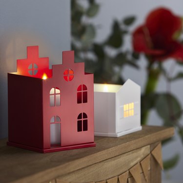 A red candle holder and a white candle holder shaped like houses on a wooden surface.