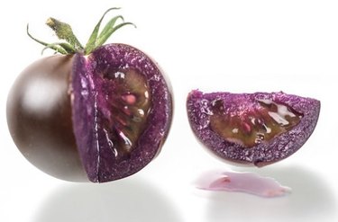 Purple tomato with a slice cut out of it on a white background.
