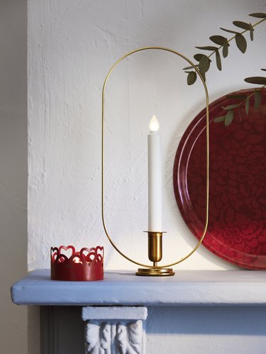 A single white electric candle in a golden stand that circles the candle like a halo.