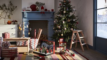 Decorated Christmas tree next to a blue fireplace surrounded by wrapping paper and presents.