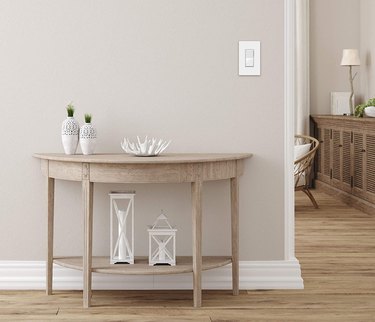 White Decorator Paddle Rocker Light Switch on Pale Gray Wall With Table and View Into Adjacent Room