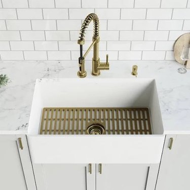 A brass sink grid inside a rectangular apron sink and a brass faucet