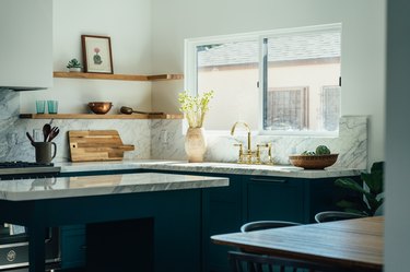 Blue kitchen with marble counters and a brass faucet