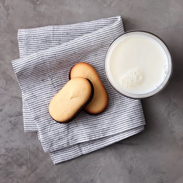 Two Milano cookies on a blue striped cloth next to a glass of milk.