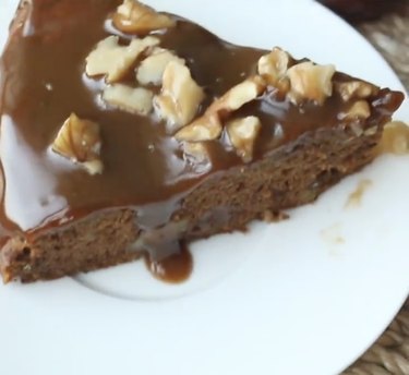 A slice of chocolate caramel date cake topped with walnuts on a white plate.