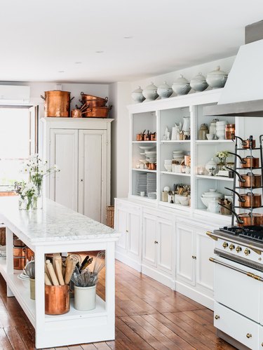 White kitchen with open shelving and stacked copper pots.