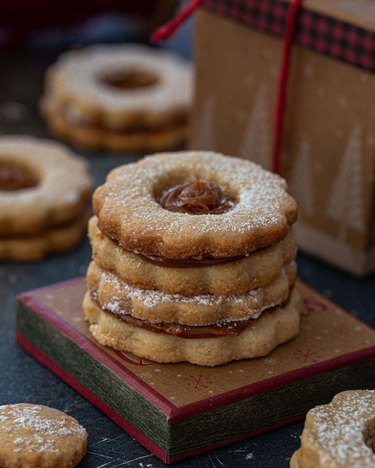 Two dulce de leche linzer cookies stacked on top of each other with more cookies in the background.