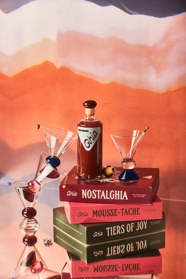 A bottle of Ghia on a pile of books with martini glasses staged around