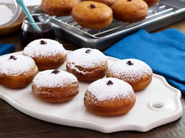 Six jelly donuts topped with powdered sugar on a white tray.