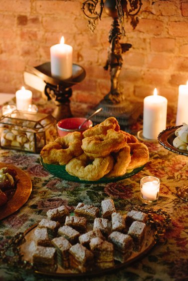 A plate of Moroccan donuts among other desserts, white candles, and plates in front of a brick wall.