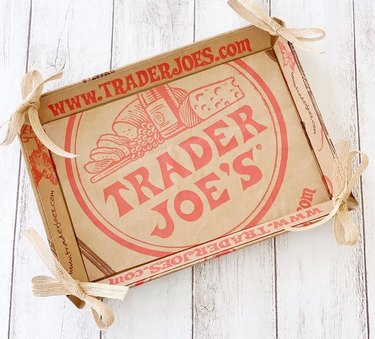 Trader Joe's cardboard box with the logo and website on a white wooden surface.