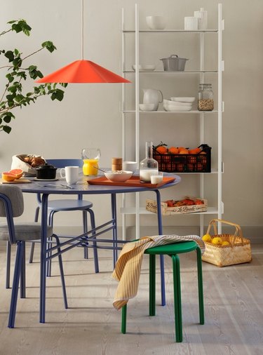 A hanging light fixture in red in a white kitchen over a blue table with a green stool.