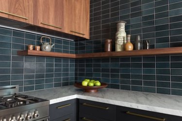Black and natural wood cabinets with marble counters and teal subway tile backsplash.
