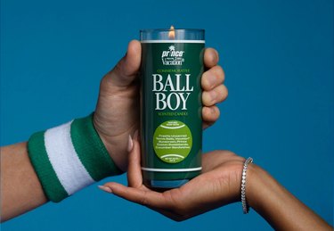 A "Ball Boy" candle being held by two hands on a blue background.
