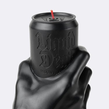 Black candle with a red wick shaped like a Liquid Death can with a hand holding it.