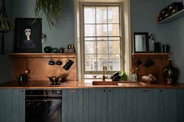 Dark green kitchen cabinets with copper backsplash.