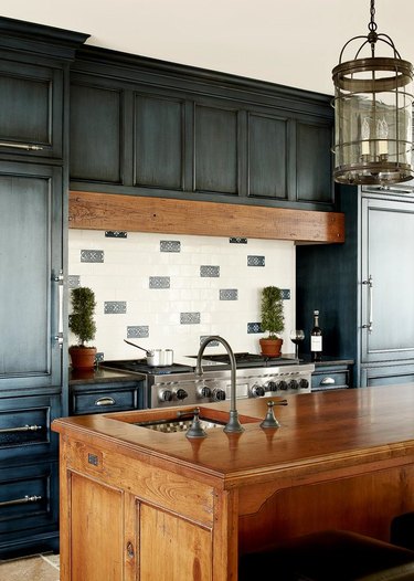 Kitchen with dark wood island, dark green cabinets, tile backsplash
