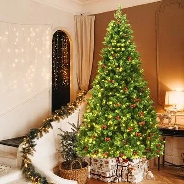 A lit Christmas tree in a living room with a white staircase