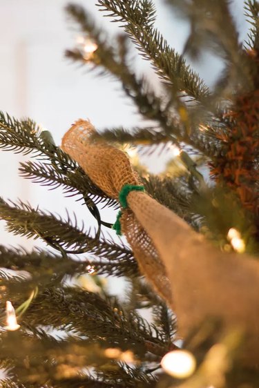 A burlap ribbon is being secured to a Christmas tree