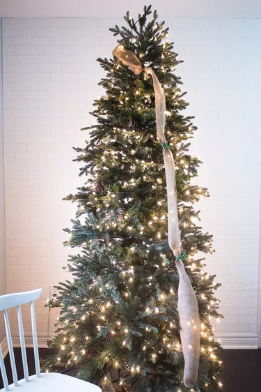A burlap ribbon is wrapped around a Christmas tree