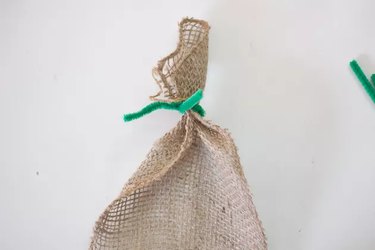 A green pipe cleaner is wrapped around burlap ribbon