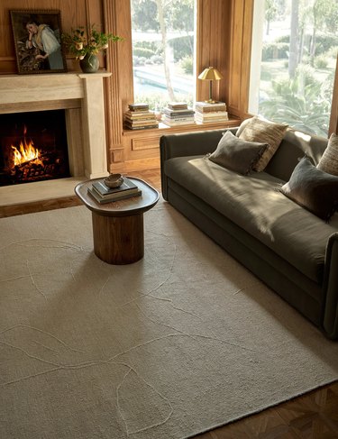 A cream-colored rug featuring a raised abstract pattern in a living room with a lit fireplace and a moss-colored couch.