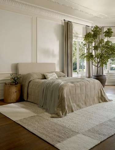 A color-blocked white and gray rug beneath a bed with a very light brown checked duvet cover.