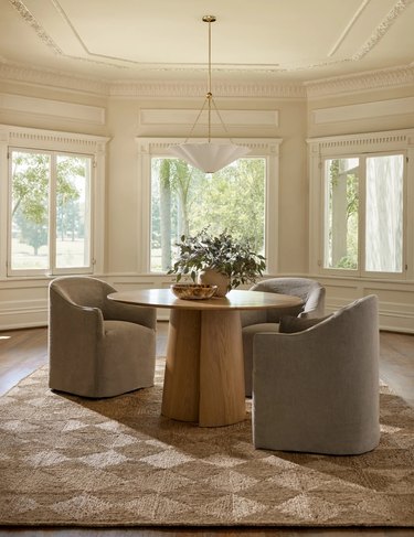 A light brown checkered rug beneath a dining table with three chairs covered in light gray fabric.