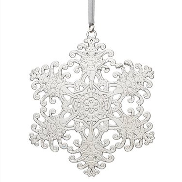 An ornate silver snowflake Christmas tree ornament, featuring intricate swirls and texture, it hangs on a silver chord.