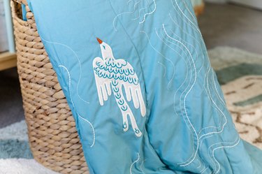 A bright blue quilt with white, wind-like lines and a white bird flying across it.