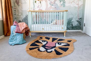 A tiger-shaped rug on a light gray carpet in front of a light blue and wood crib.