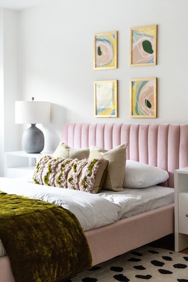 bedrom area with pink velvet bed and four framed artworks