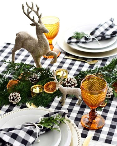 tablescape with black-and-white plaid linens, orange glasses, cedar and orange decorations, and sparkly reindeer