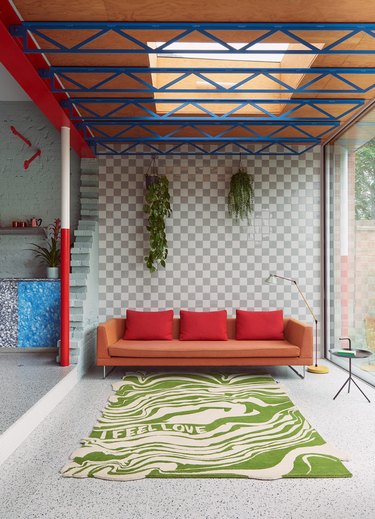 open plan living space with checkerboard wall, orange sofa and statement trippy rug