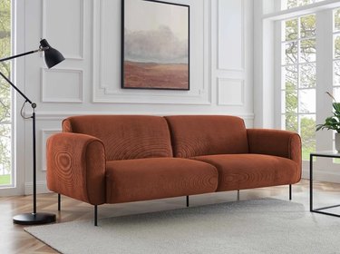 Wayfair's Upholstered Sofa in orange on a wooden floor in front of a white wall.
