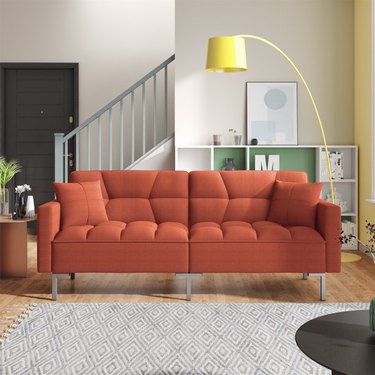 Walmart's Convertible Futon Sofa bed in orange on a wooden floor in a living room.
