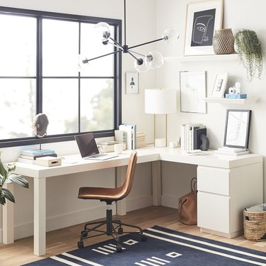 white wrap-around desk with lighting fixture and shelves and windows nearby