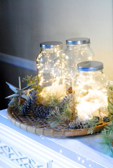 Vignette of fairy lights in mason jars surrounded by pinecones, pine sprigs and a metal star.