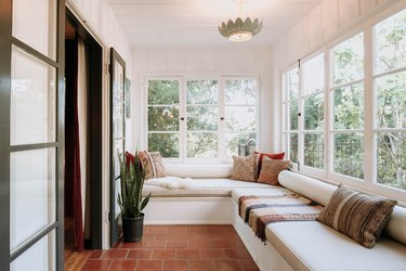 A sunroom with a white bench seating and a snake plant on a brick floor