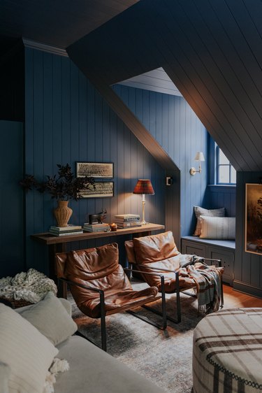 Living room with blue walls, leather chairs, plaid ottoman and moody lighting