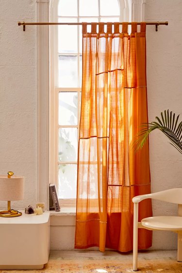 Orange gauze curtain, accent chair, plant, rug, lamp.