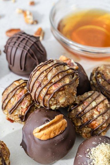 Pecan Pie Bourbon Balls on a white countertop, with some drizzled with chocolate with others are coated in it.